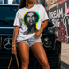 Woman wearing a graphic t-shirt with a colorful design, sitting in front of a black Mercedes-Benz SUV.
